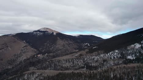 Drohnenschwenkaufnahme-Eines-Schneebedeckten-Berggipfels-Mit-Wolken-Und-Blauem-Himmel