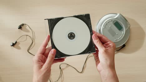 hands holding a cd, next to a cd player and headphones