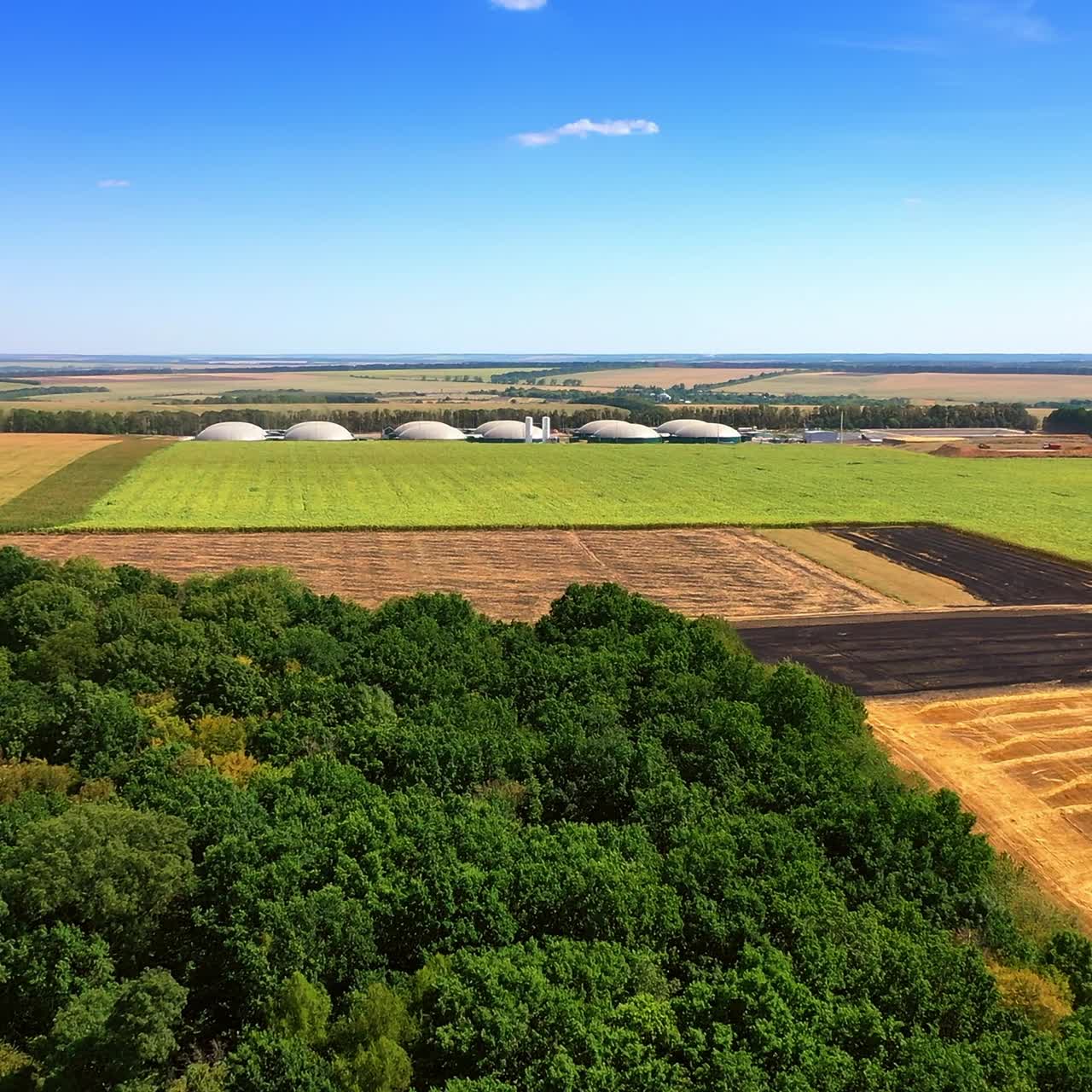 Drone flight over the green woods and fields to the tanks of biogas plant. Sustainable production of green energy