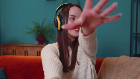 Una-Joven-Muy-Alegre-Con-Auriculares-Inalámbricos-Bailando,-Cantando-En-Un-Acogedor-Sofá-En-El-Salón-De-Casa