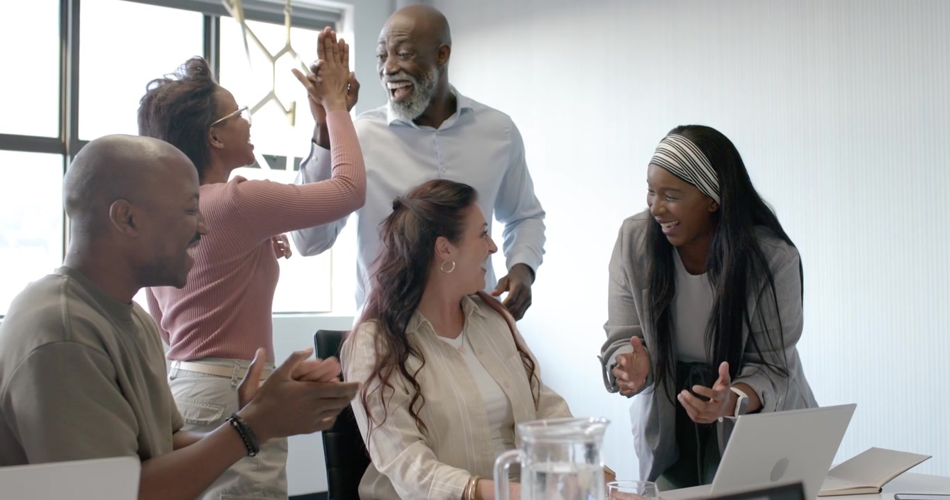 Diverse team in business wear celebrating laptop chart success with seated woman pointing in office