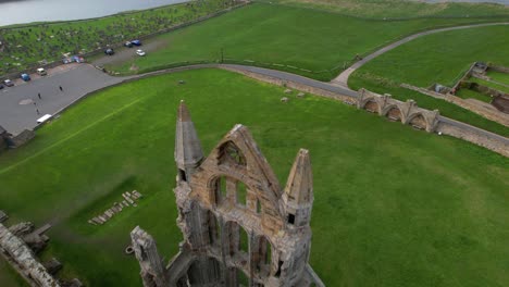 aerial backward tilt up reveal over whitby abbey ruins with port and lighthouse in background, north yorkshire in england