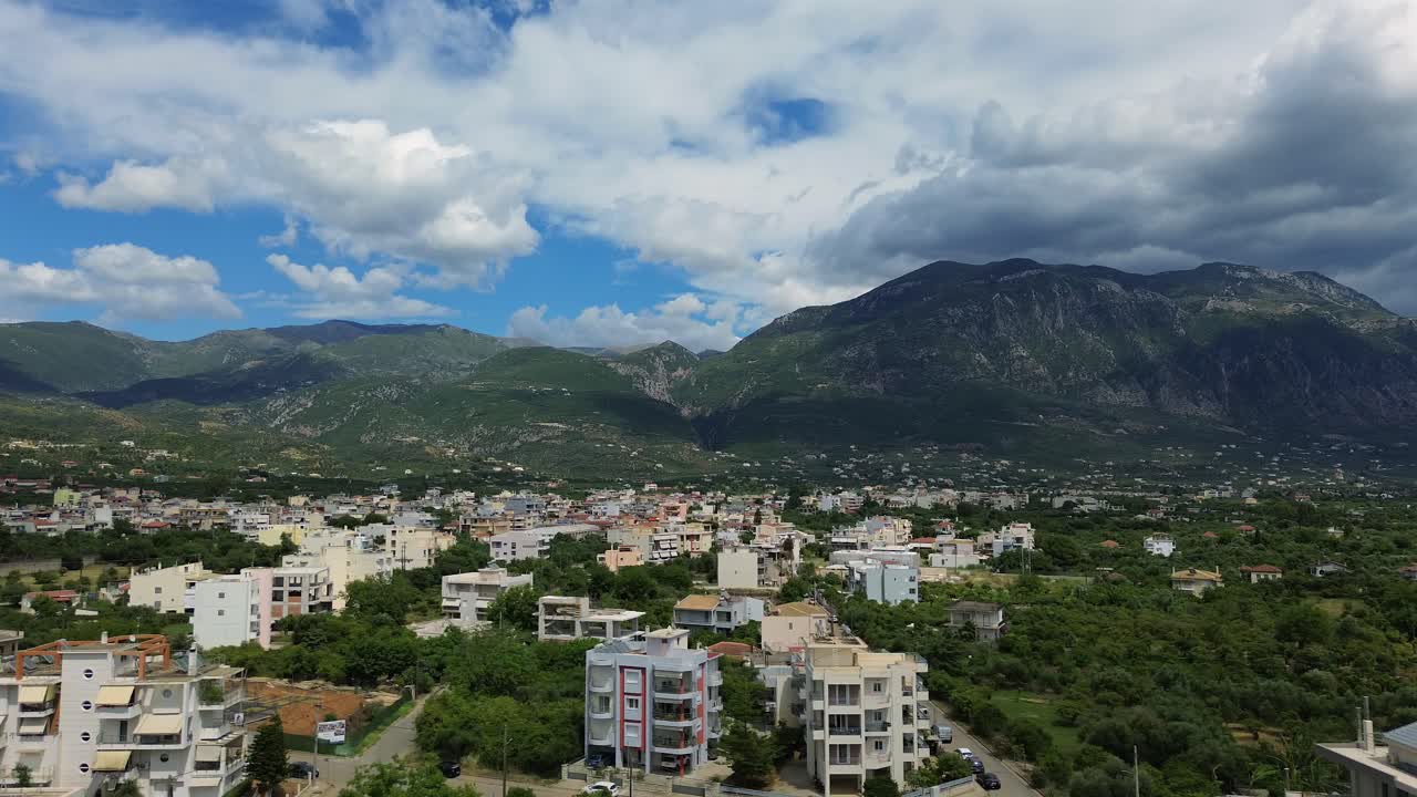 Aerial wide panoramic view of eastern suburbs of Kalamata, left slide dolly shot, Taygetos mountain on background, blue sky with beautiful cloud formations, 4K