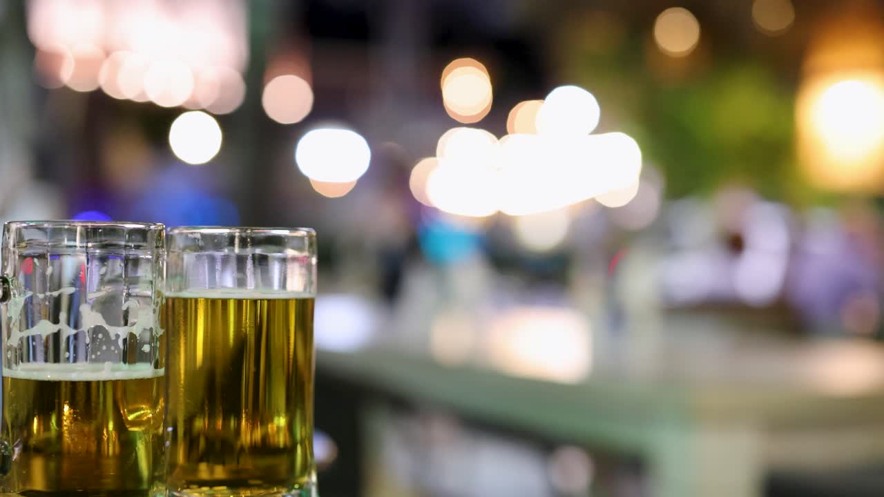 Blurred nighttime scene with beer glasses in focus, capturing movement and vibrant lights in a lively setting