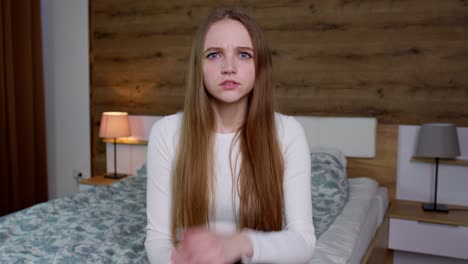 young woman with long blonde hair smiles and talks to the camera in a bedroom