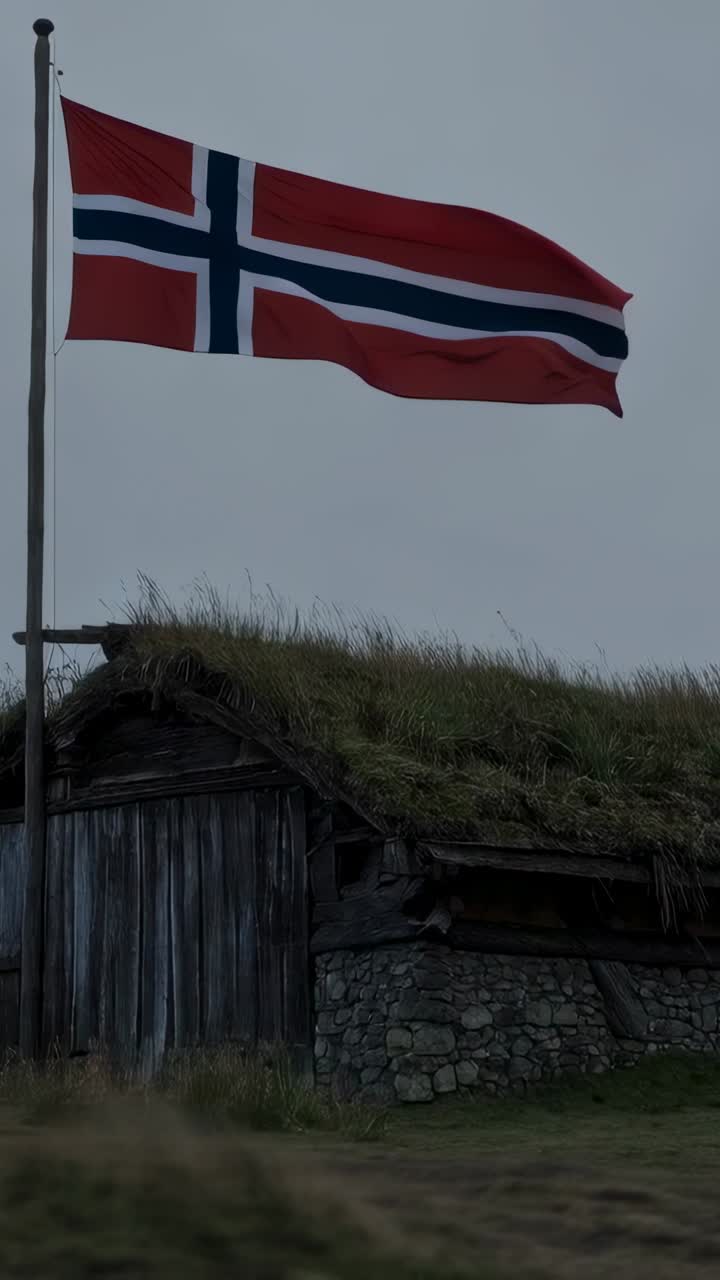 Vertikal video: Viftende norsk flagg på stang som folder seg ut i kraftig vind ved en bygning med torvtak