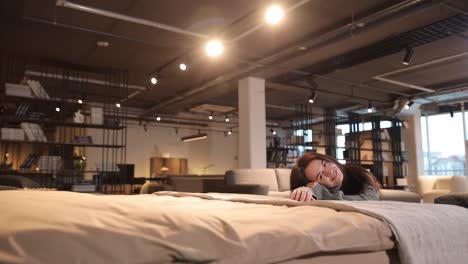 smiling woman testing softness of new mattress in modern furniture showroom smiling woman testing softness of new mattress in modern furniture showroom high quality footage