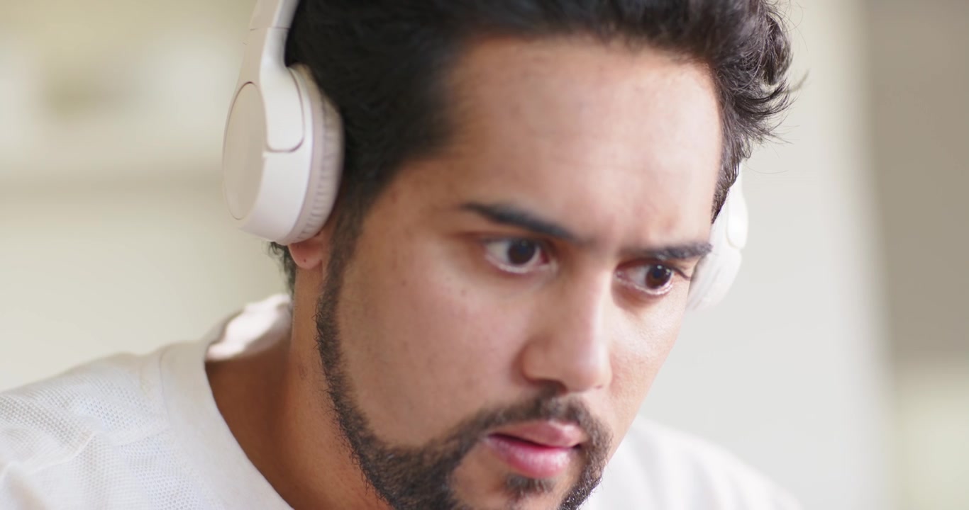 自宅でヘッドホンを着用し、音声キューを聞きながらノートパソコンに身を乗り出し集中しているアフリカ系アメリカ人男性。