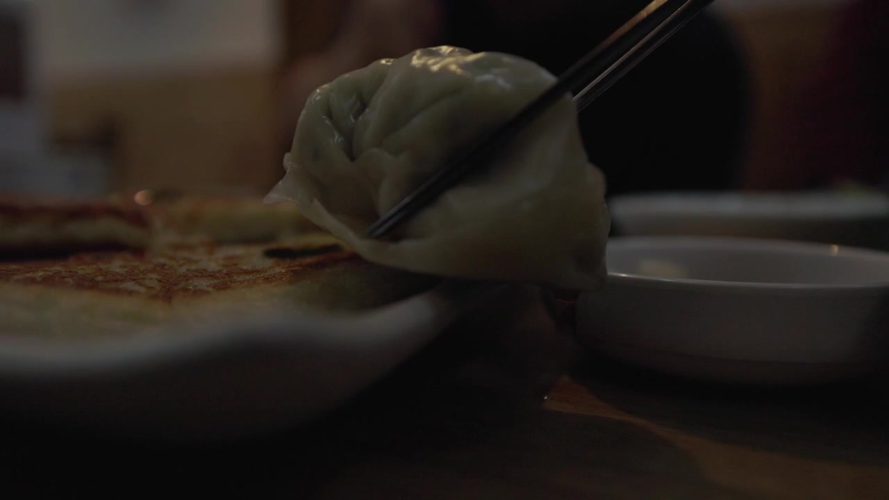 A Traditional Korean Dumpling Held With Chopsticks, Food And Utensil In Close-up View.