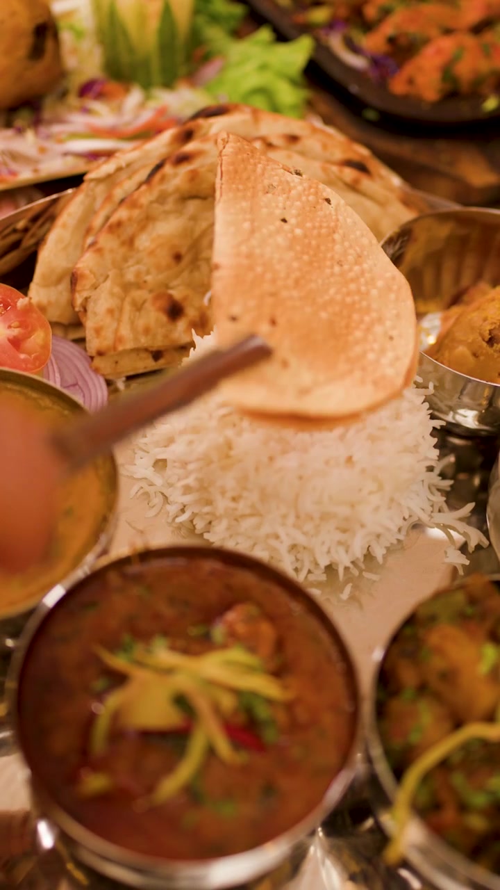 Primer plano de un plato thali de metal que contiene varios curries, arroz y pan papadum crujiente.