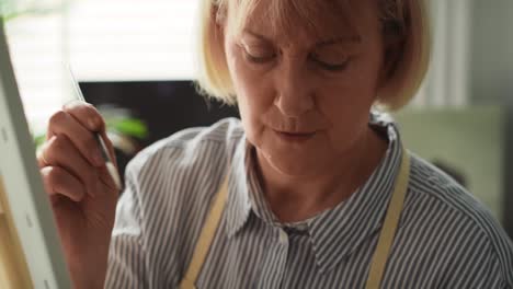 Close-up-video-of-senior-woman-painting-at-easel.