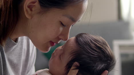 an asian woman kisses her newborn baby girl's forehead a few months old