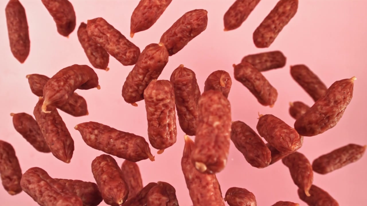 Mini kiełbaski salami spadające na różowe tło