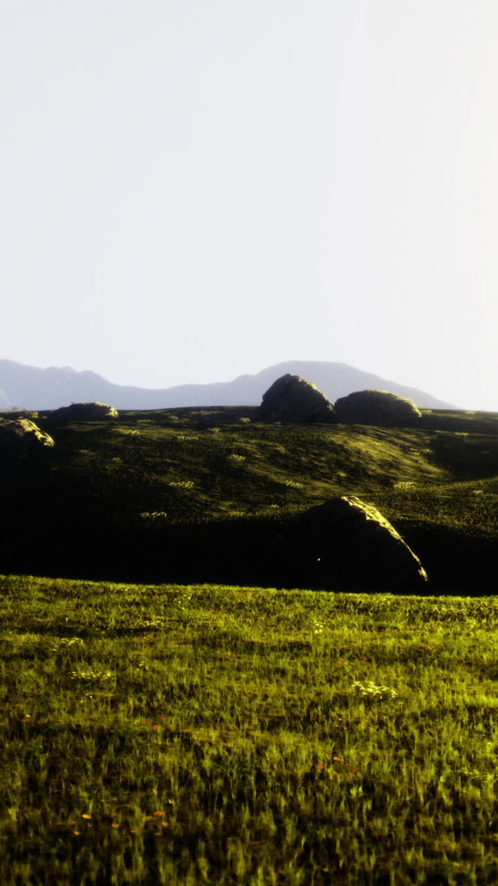 Serene landscape with rolling hills and distant mountains under sunlight