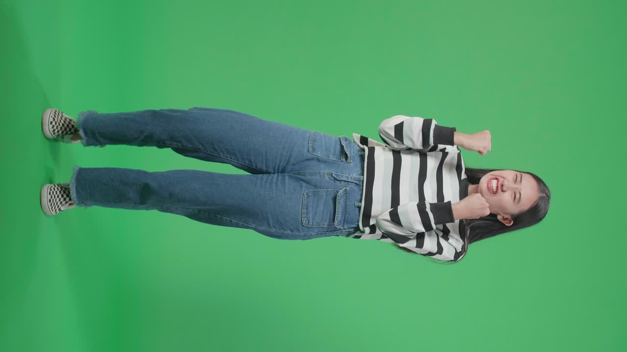 Full Body Of A Happy Asian Woman Celebrating While Standing In Front Of Green Screen Background