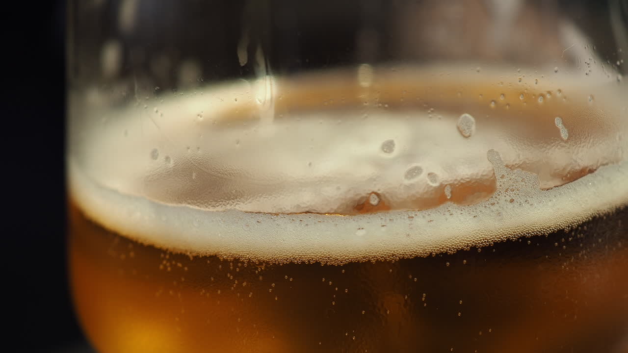 Person puts down golden foamy cup of Beer on a table after sipping it - Close up