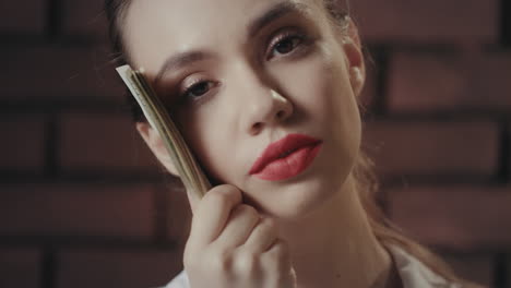 thinking woman holding money stack near face and looking into camera