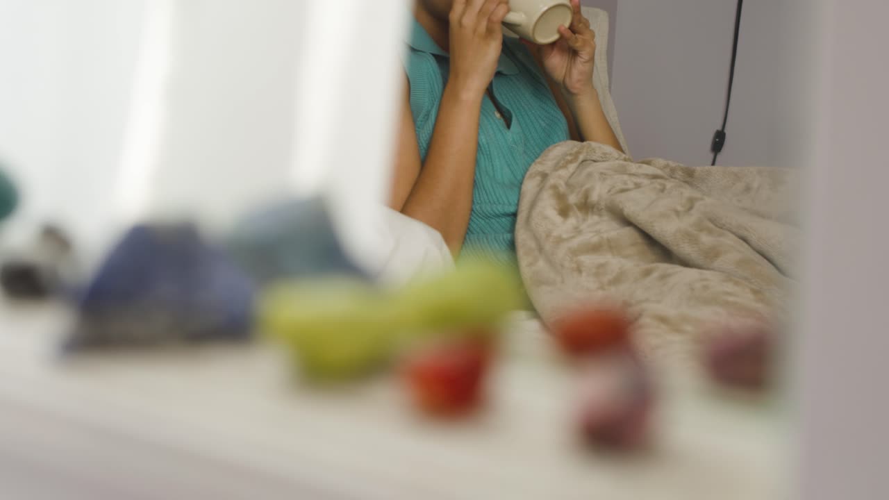 mujer del sur de asia bebiendo té en la cama, cristales borrosos en primer plano