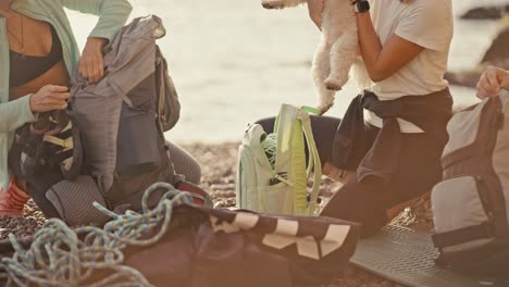 Close-up-shot-of-a-group-of-rock-climbers-laying-out-their-backpacks-and-taking-out-the-necessary-equipment-for-chopping-and-pounding-the-rocks-near-them-their-dog