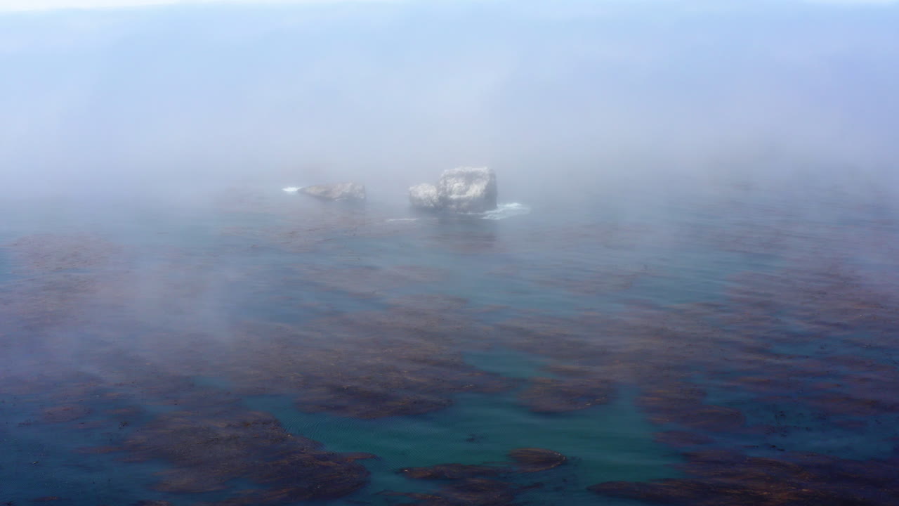 enormes rocas que sobresalen del mar, apenas vistas a través de la niebla que fluye sobre el agua