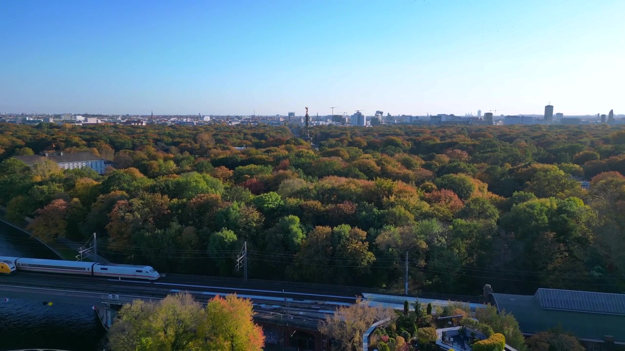 Ikonický berlínský Vítězný sloup tyčící se nad zářivým podzimním listím parku Tiergarten, s panoramatem města v pozadí. Majestátní letecký záběr dronu letícího vpřed
