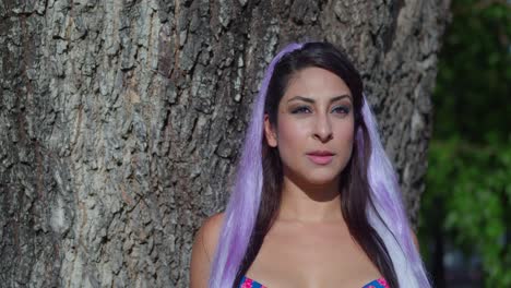 Amazing-close-up-of-a-young-woman-with-white-hair-standing-by-a-large-tree-trunk-in-the-park