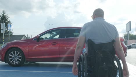 young handicapped driver getting in red car from wheelchair