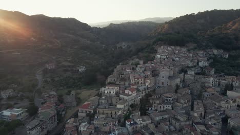 the sun sets over a mountain peak as we circle around a historic calabrian town in southern italy