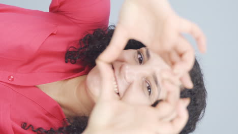 Vertical-video-of-Young-woman-making-heart-sign-at-camera.