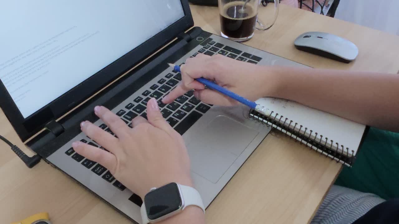 Student taking handwritten notes in a notebook during an online class or study session with a laptop