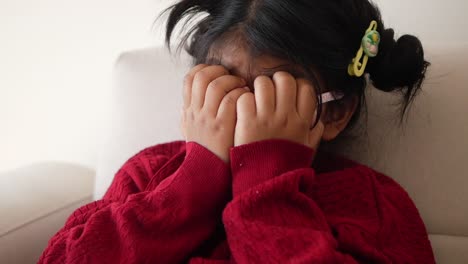 a young girl covering her eyes with her hands, appearing to be upset or sad