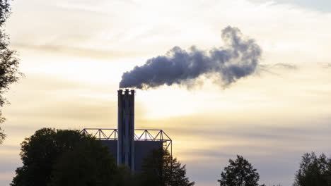 lapso de tiempo de la chimenea de la fábrica humeante contra el fondo de un sol poniente