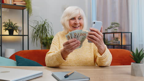 Smiling-happy-senior-grandmother-woman-counting-money-cash-use-smartphone,-income-saves,-lottery-win