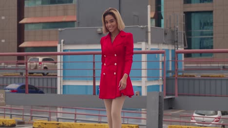 In-Port-of-Spain,-Trinidad,-a-young-girl-of-Hispanic-descent-wears-a-striking-red-dress-on-a-rooftop,-with-tall-buildings-in-the-background