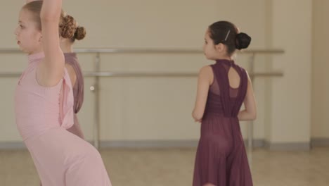 a group of young ballet students in black dancewear practicing positions in a spacious ballet studio with wooden flooring and wall-mounted barres. focused expressions and synchronized movements.