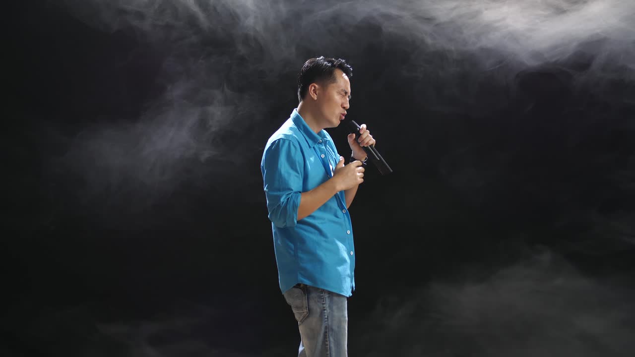 연기가 있는 무대에서 마이크를 들고 노래하는 남자