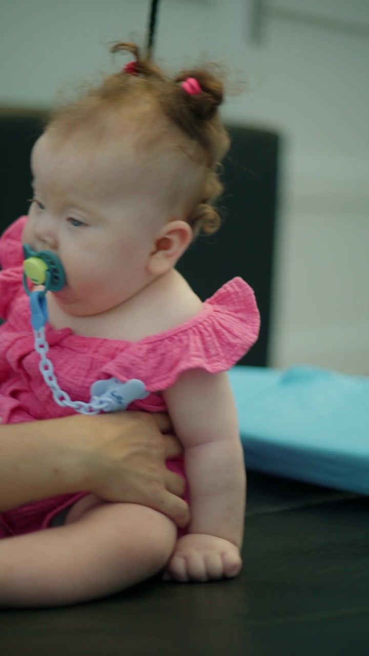 Close up of a parent's hands gently holding a newborn baby wearing a pink bodysuit and using a pacifier