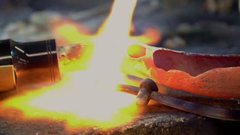 a blacksmith uses gas welding to melt a brass saxophone, resulting in destructive sparks and brightly coloured flames