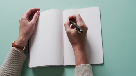 close up of hands writing with pen on book with copy space on green background in slow motion