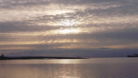 Sun-setting-behind-cloud-over-rippling-west-coast-ocean-water