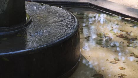 Agua-Que-Fluye-De-Una-Pequeña-Fuente-Con-Hojas-De-Otoño-En-El-Fondo