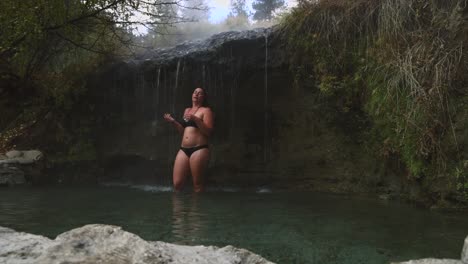 woman stands beneath a thermal hot spring waterfall enjoying the benefits of natural heated hot spring water on body in a heated pool in nature in pacific northwest