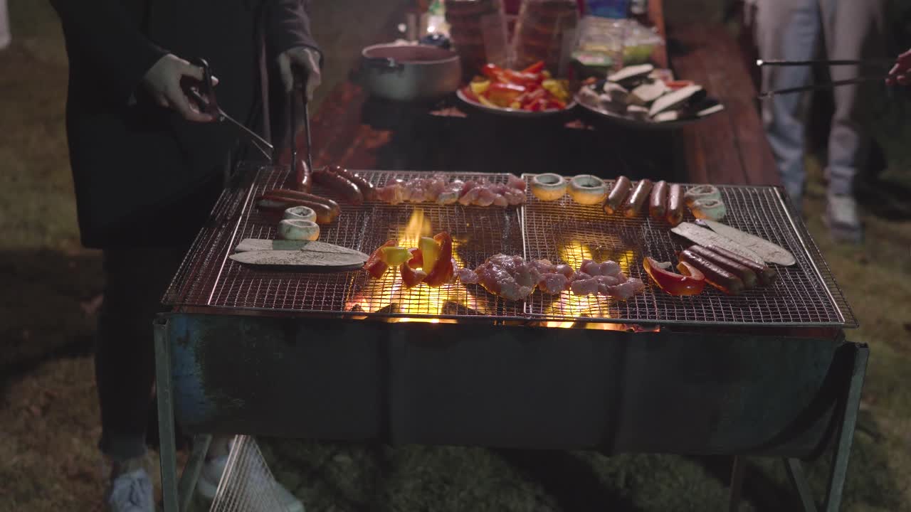 바비큐 앞에 서서 정원에 있는 집 앞 버섯, 소시지, 닭고기, 가지를 굽는 사람들