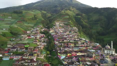aerial trucking shot of beautiful village of nepal van java in indonesia during sunny day - plantation and cultivation of fields on slope and colorful village located on cliff