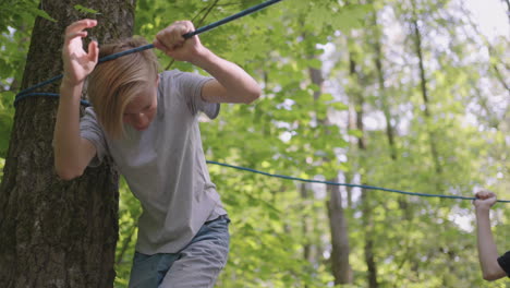 small boy in climbing equipment in a rope park. group of caucasian children training at boot camp. in the children camp children are taught to overcome obstacles with the help of a rope crossing