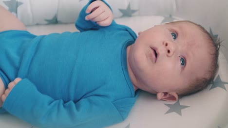 small-child-in-blue-bodysuit-kicks-bare-legs-lying-in-cocoon