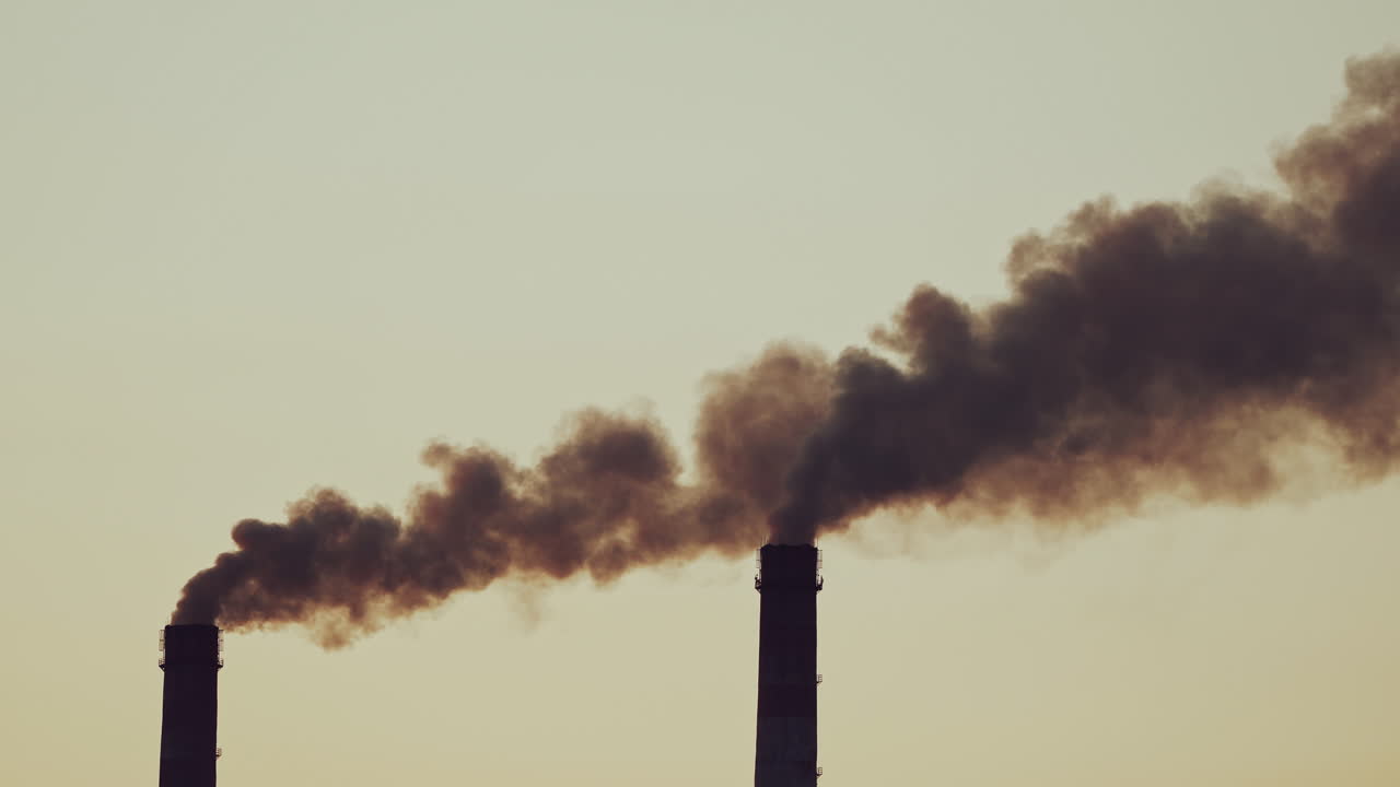 Two pipes with thick dirty smoke filling the air. Dark fumes going from the factory pipes on the sky background. Pollution of the environment.