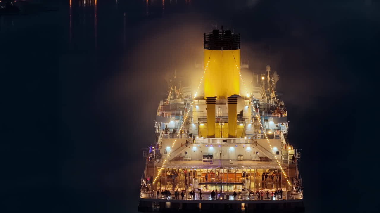 Aerial drone view of a massive cruise ship, brightly lit with warm lights, as passengers enjoy its outdoor decks at night