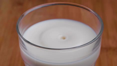 Zeitlupe-Eines-Tropfens-Milch,-Der-In-Ein-Glas-Milch-Auf-Einem-Tisch-Spritzt,-Nahaufnahme-Von-Oben,-Statische-Studioaufnahme