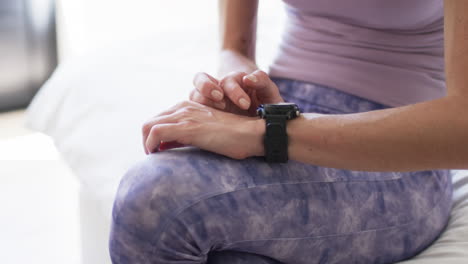 Middle-aged-Caucasian-woman-checks-her-smartwatch-during-a-workout-at-home